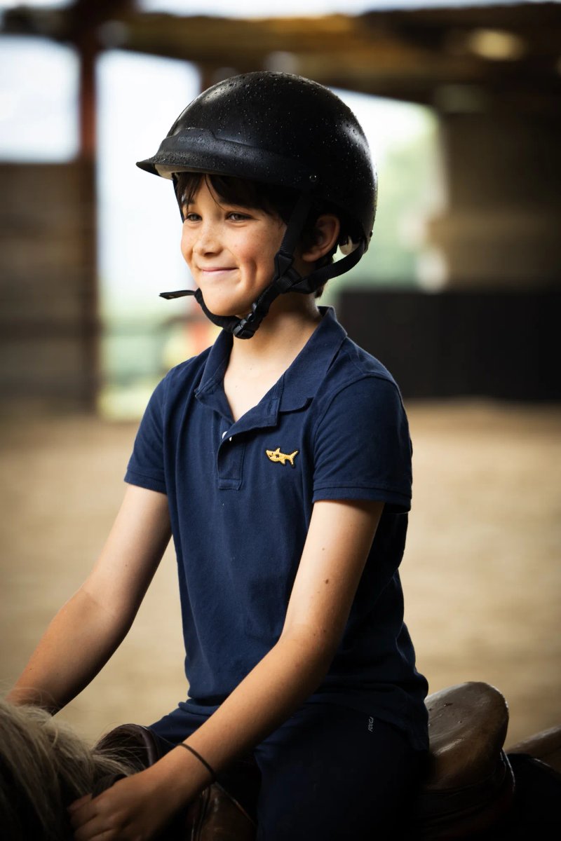 Jeune garçon souriant à cheval, portant un casque et un polo.