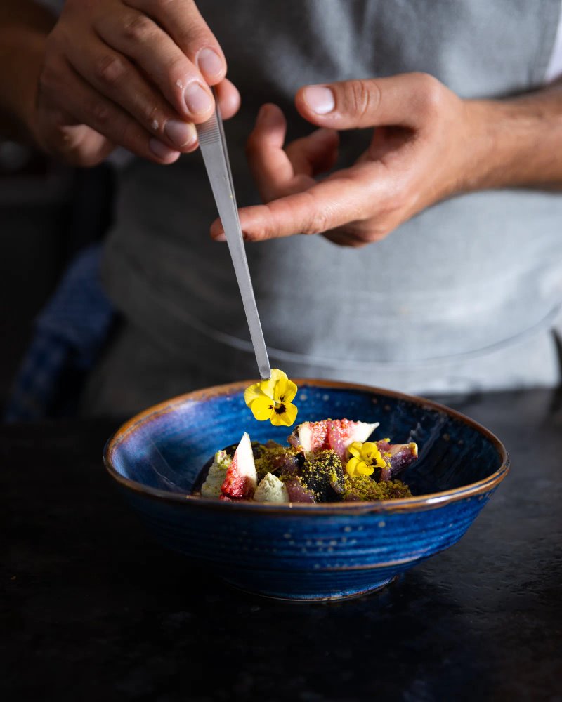 Chef ajoutant une fleur jaune à un plat de figues et pistaches.