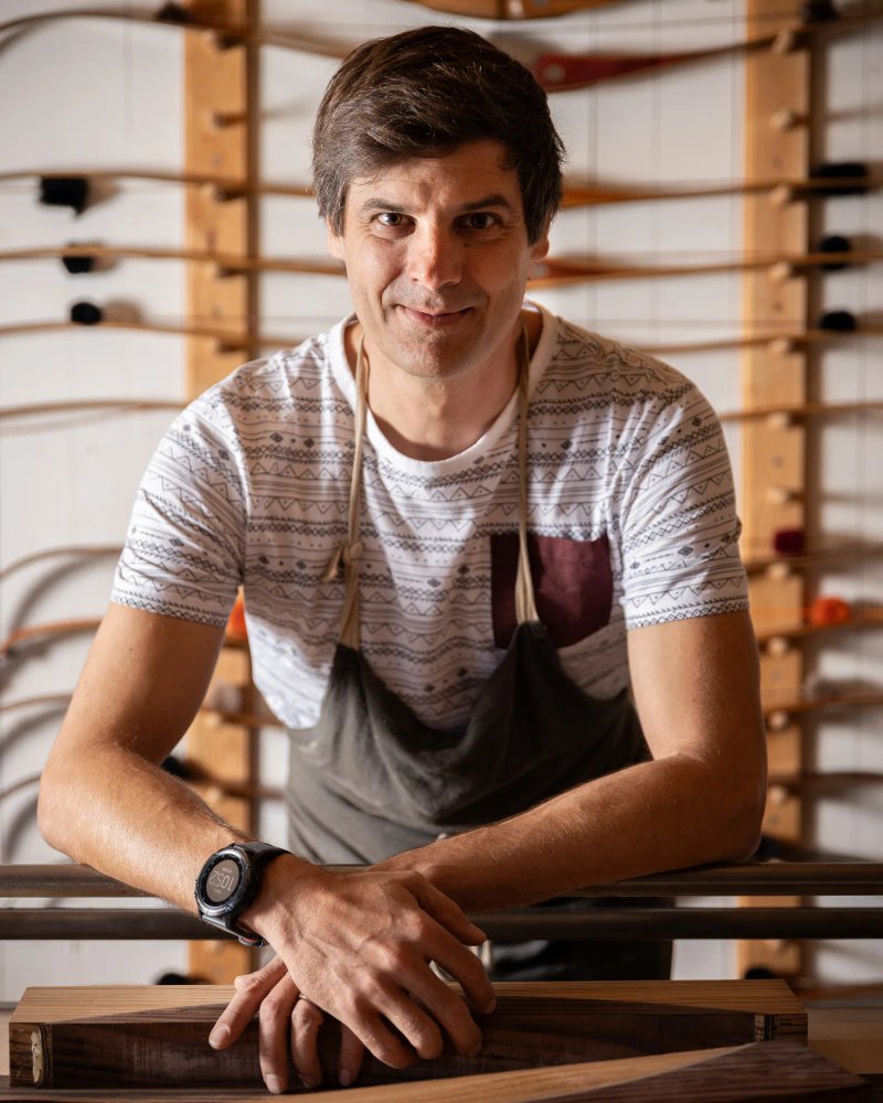 Portrait rapproché d’un homme souriant, les bras croisés sur une surface en bois.
