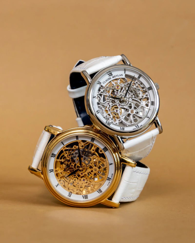 Deux montres squelette Claude Meylan en finitions dorée et argentée sur fond bronze.