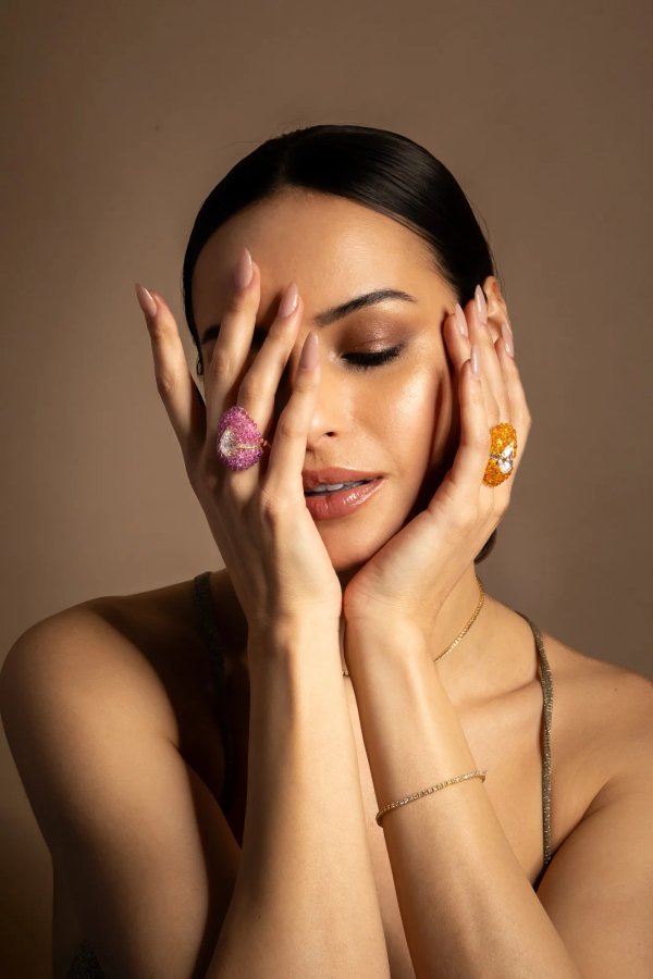 Femme maquillée cachant son visage de ses mains, portant deux bagues et un bracelet.